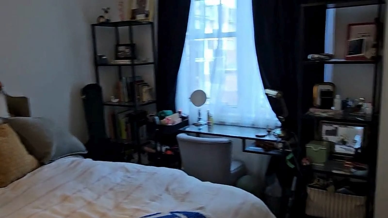 A still from a customer's phone walkthrough: a bedroom with the bed, shelving unit and a desk by the window.